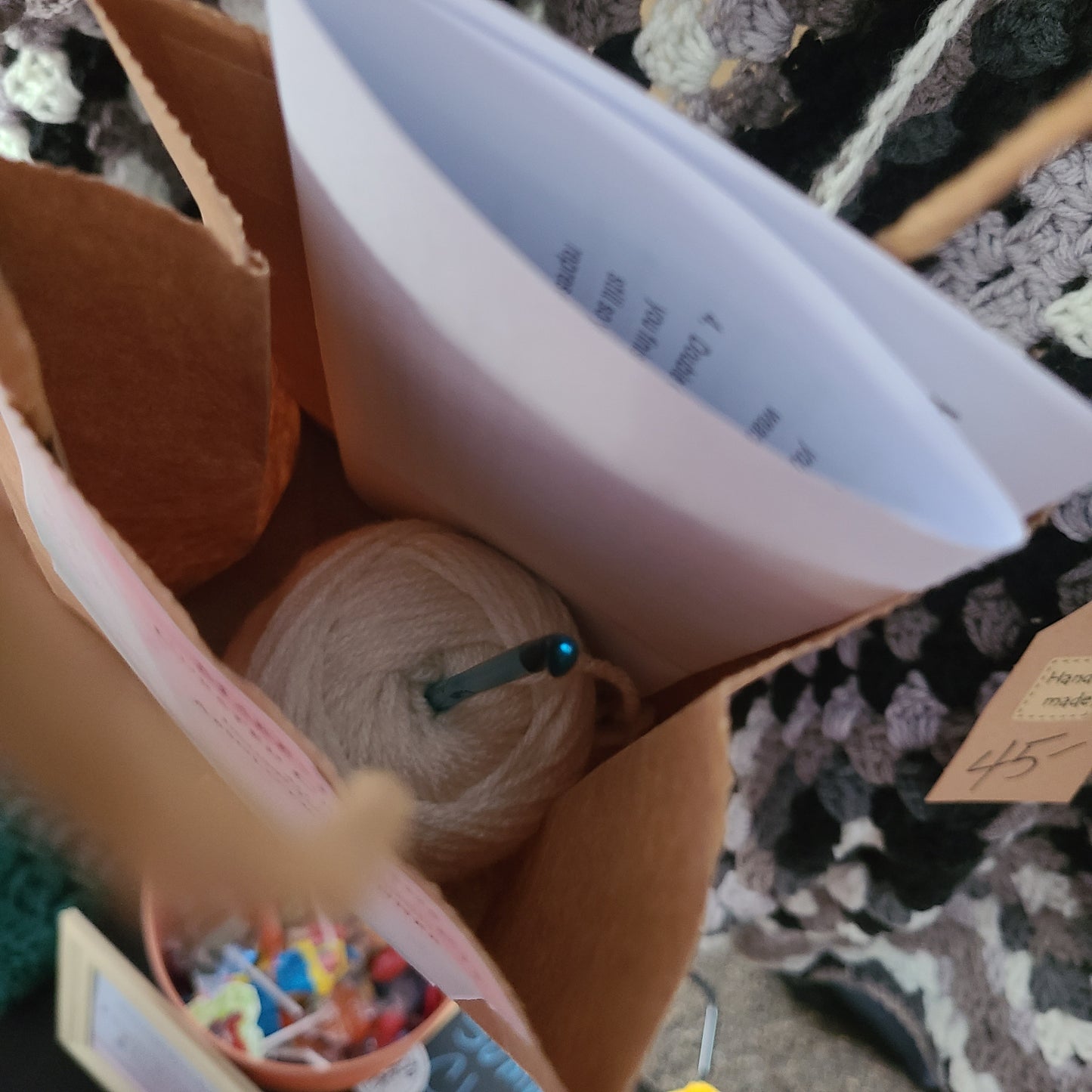 Beginner crochet starter kit in a kraft project bag, including yarn, crochet hook, and printed beginner instructions.