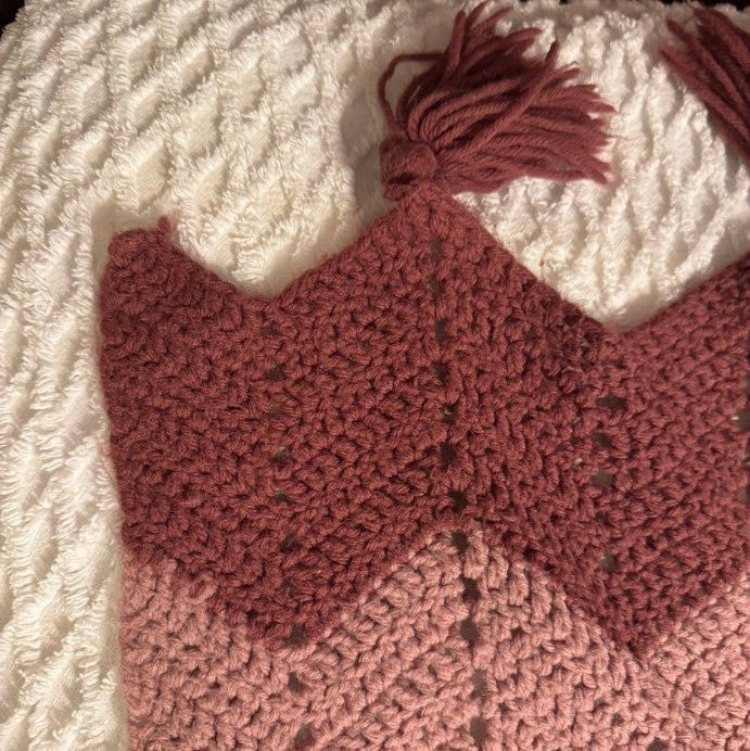 Crocheted pink heart with tassel on a textured fabric background