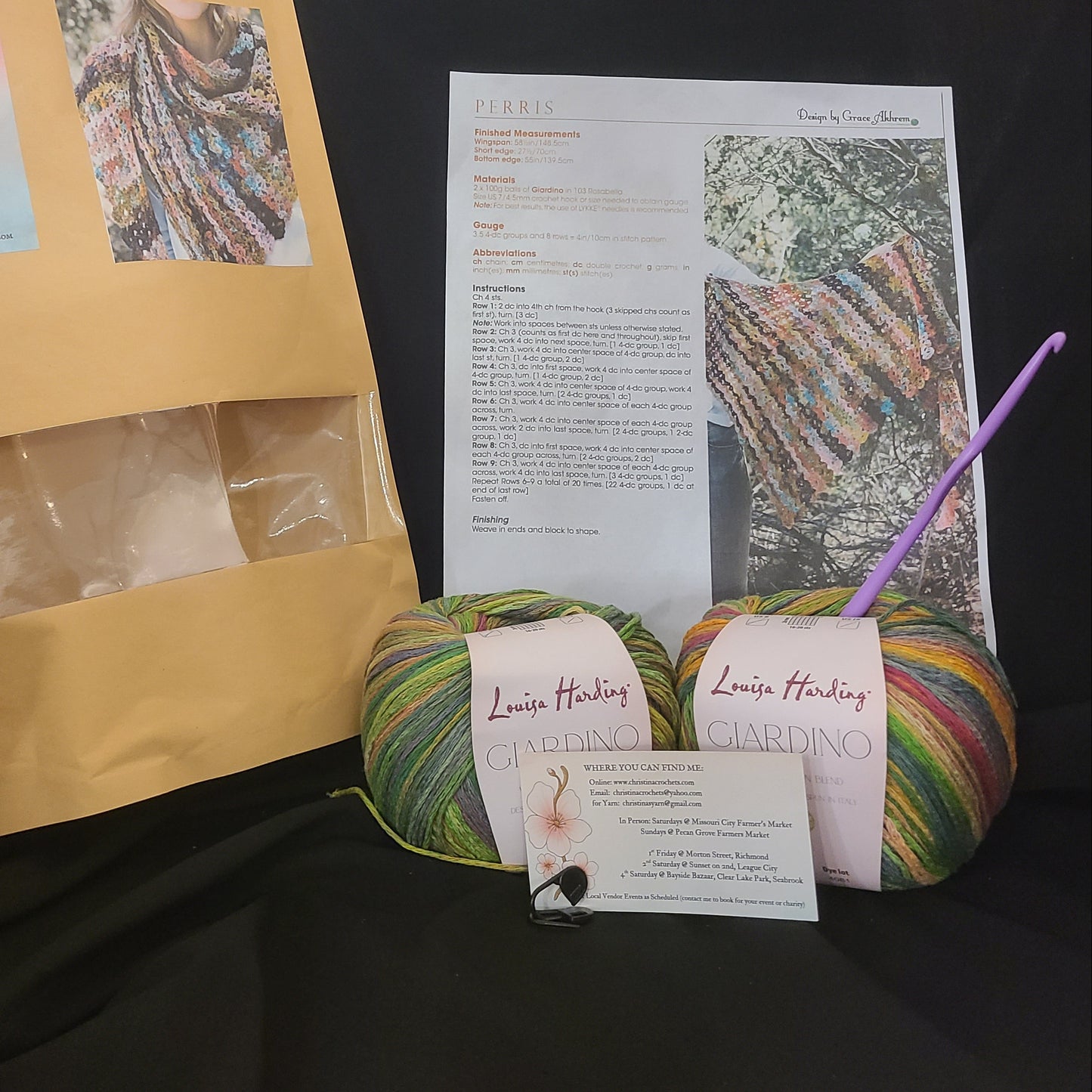 Yarn ball with a purple crochet hook, pattern sheet, and open cardboard package on a dark surface.