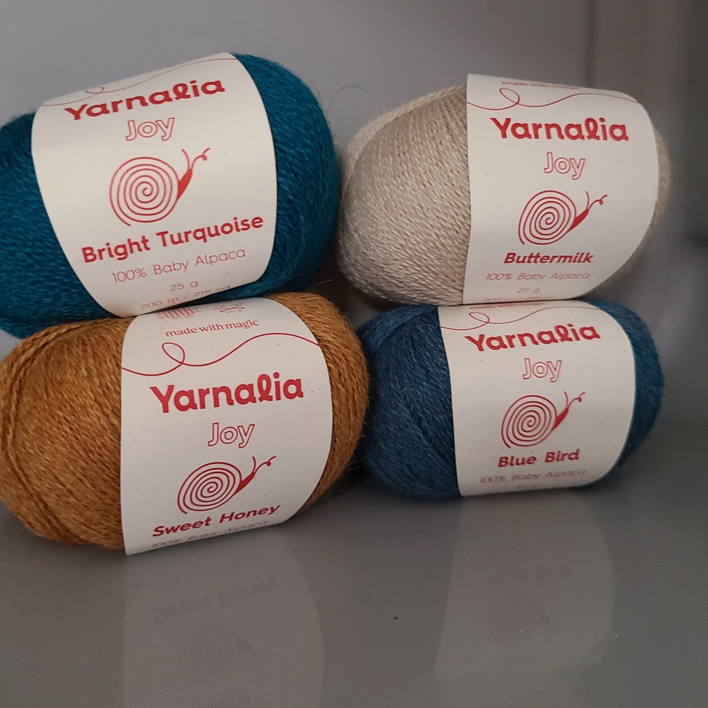 Four balls of yarn with Yarnalia labels Buttermilk, Bright Turquoise, Sweet Honey, Blue Bird