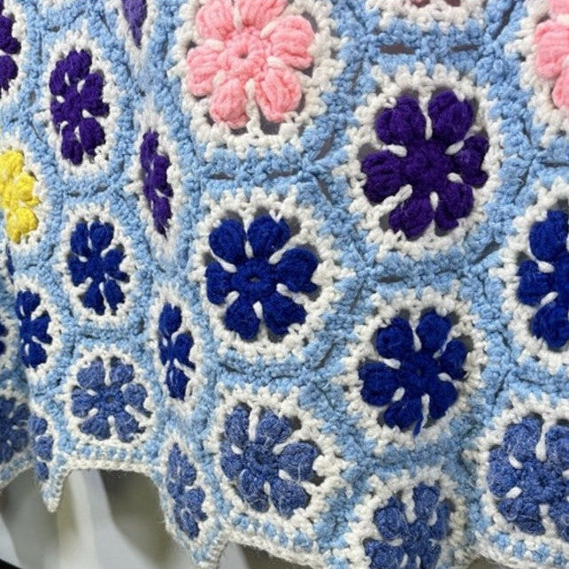 Colorful crocheted blanket with a geometric pattern on a bed.