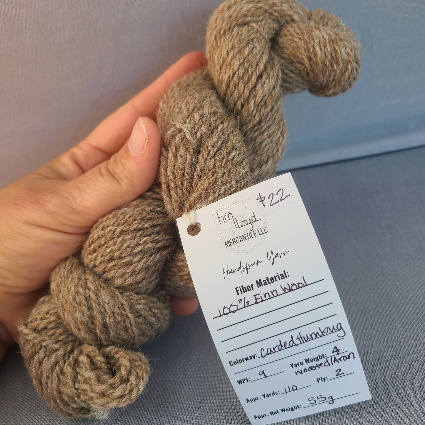 Hand holding skein of yarn with a label against a gray background