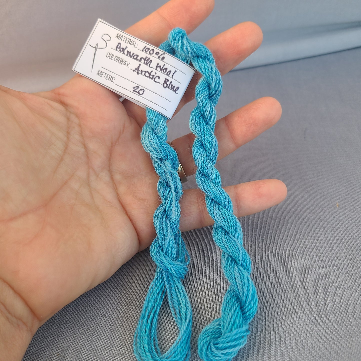 Blue yarn held in a hand with a label on a gray background