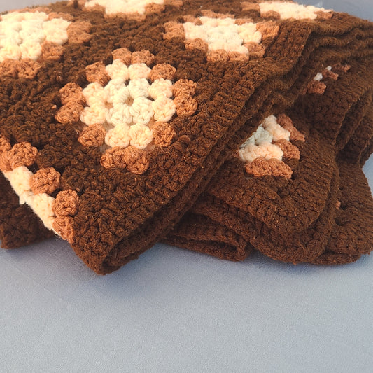 Brown and beige crocheted blanket on a light blue background