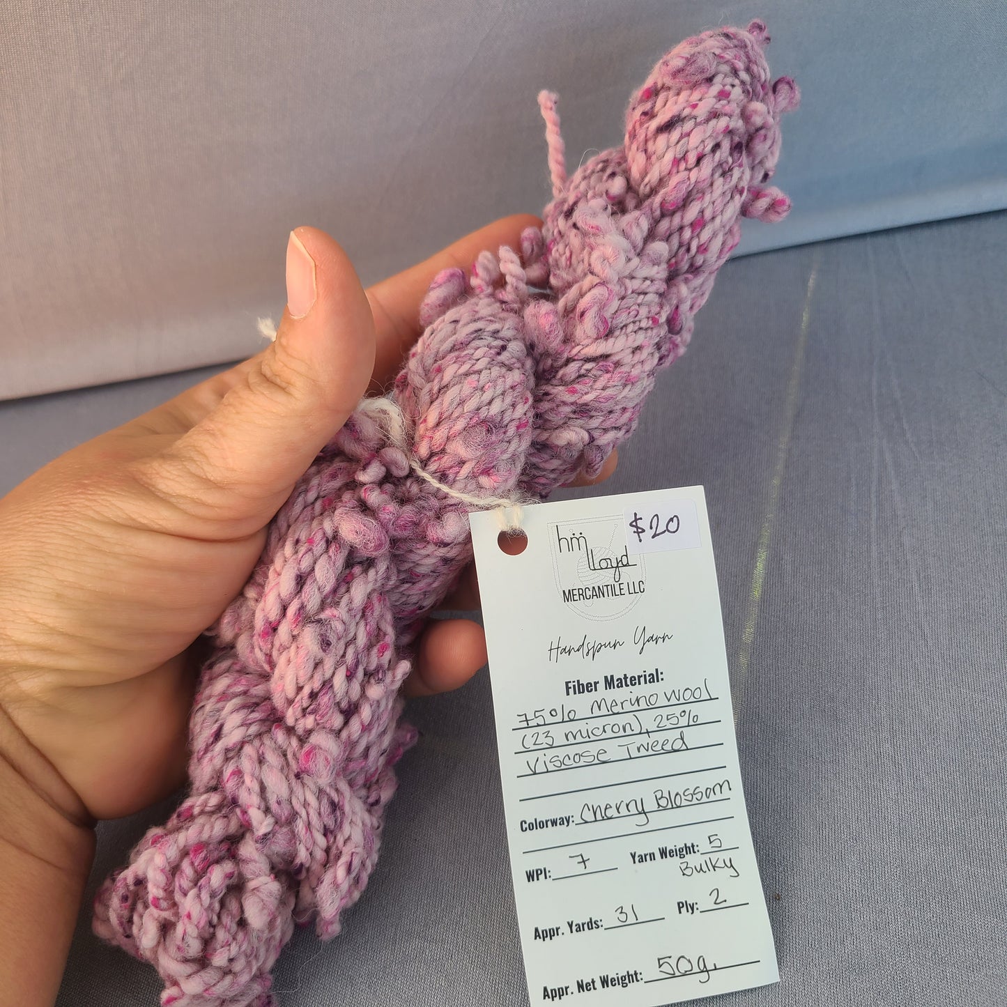 Hand holding pink yarn with a price tag against a metallic surface