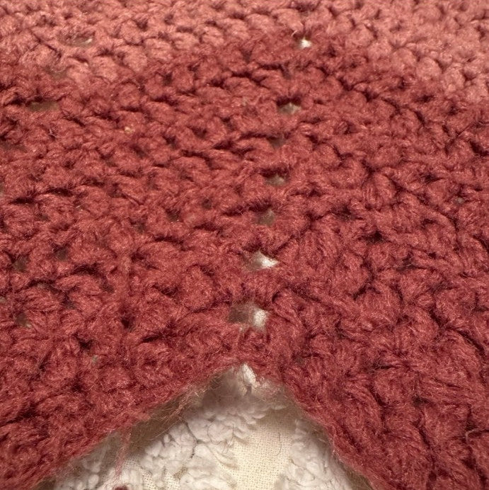 Close-up of a red crocheted fabric corner on a textured surface.