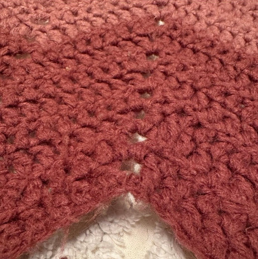Close-up of a red crocheted fabric corner on a textured surface.