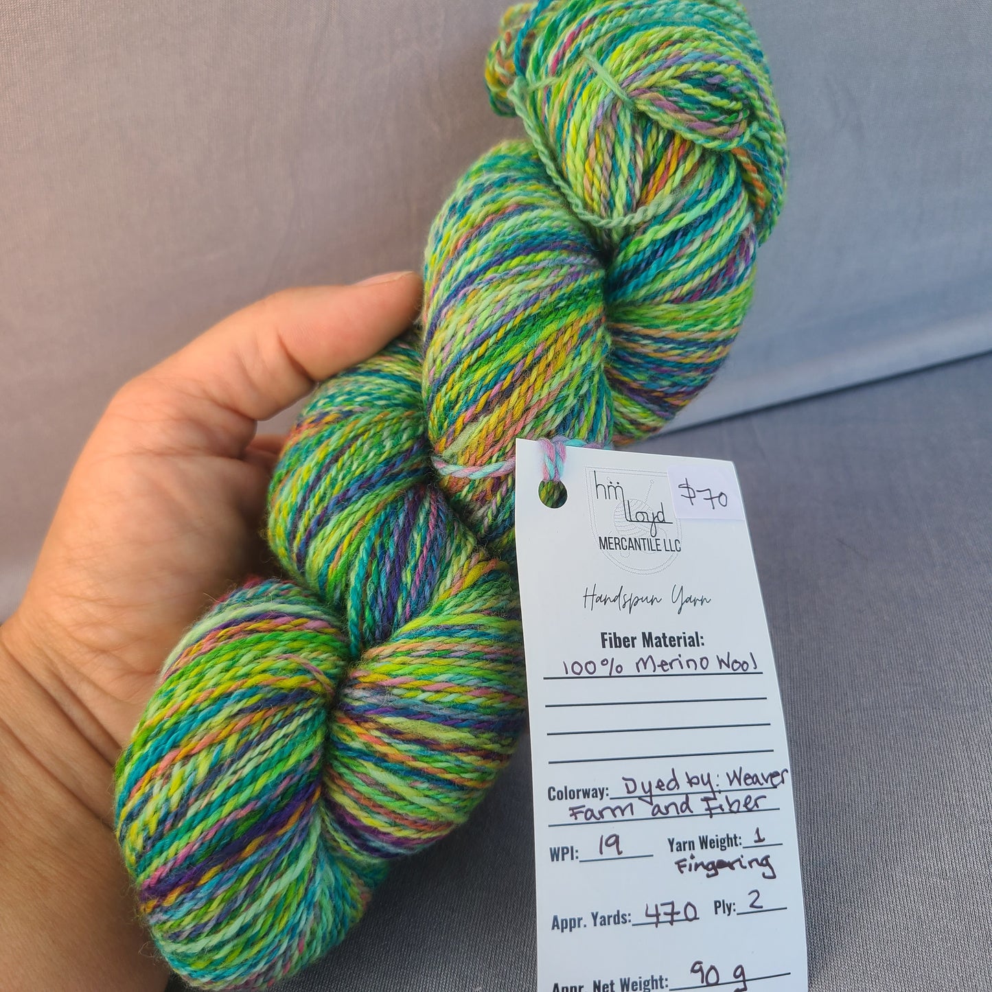 Multicolored skein of yarn held by a hand with a label on a gray surface