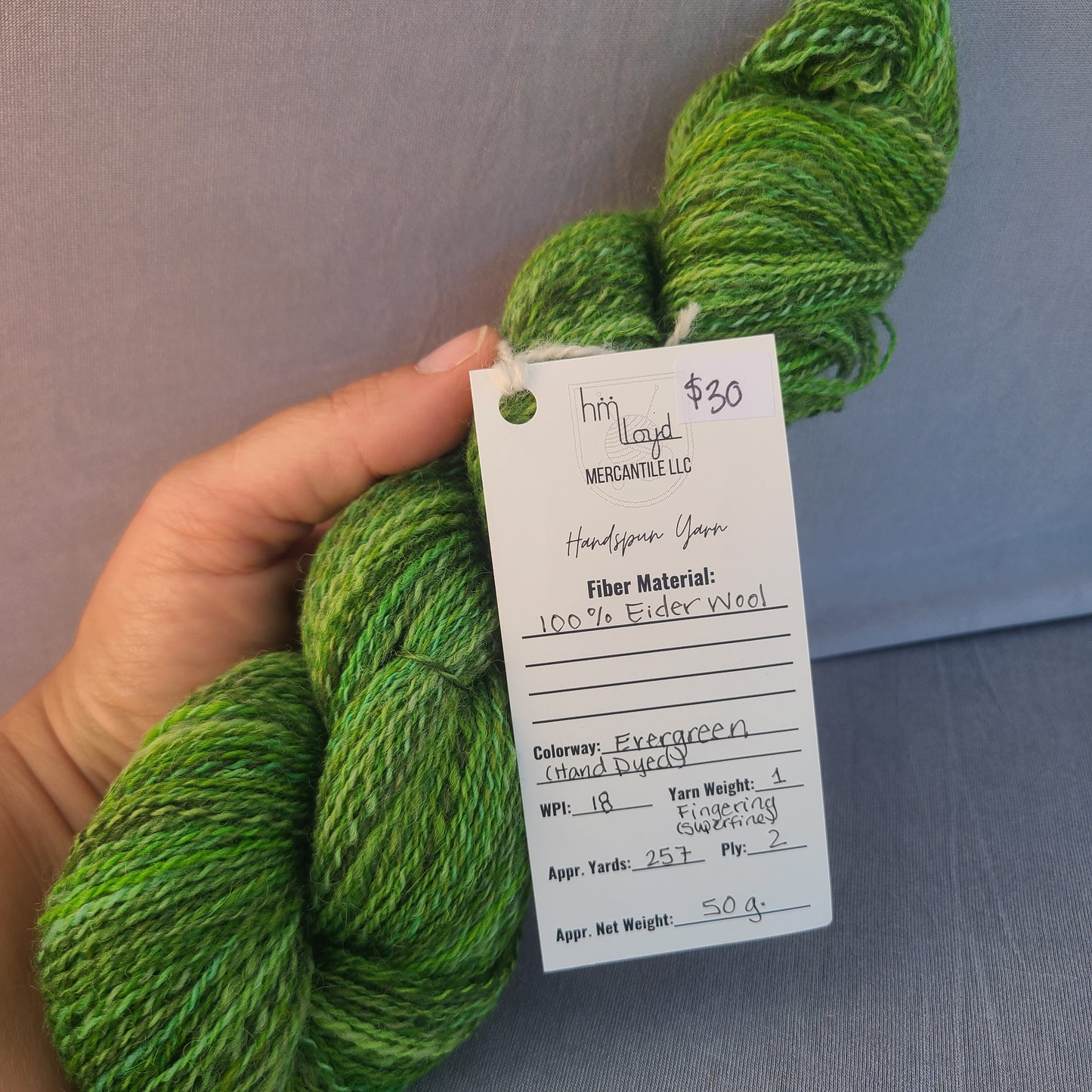 Green yarn skein held by a hand with a price tag on a metallic surface