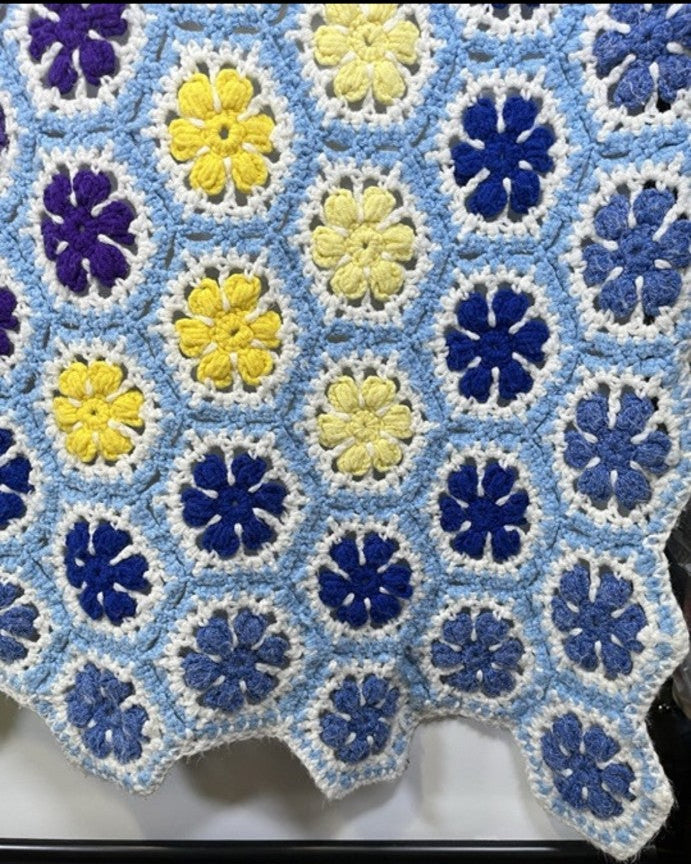 Colorful crocheted blanket with blue, yellow, and purple flowers on a white surface.