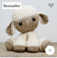 Knitted toy sheep with a white hat on a wooden surface