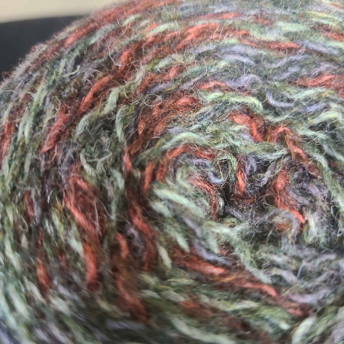 Close-up of a skein of multicolored yarn with green, orange, and gray tones.
