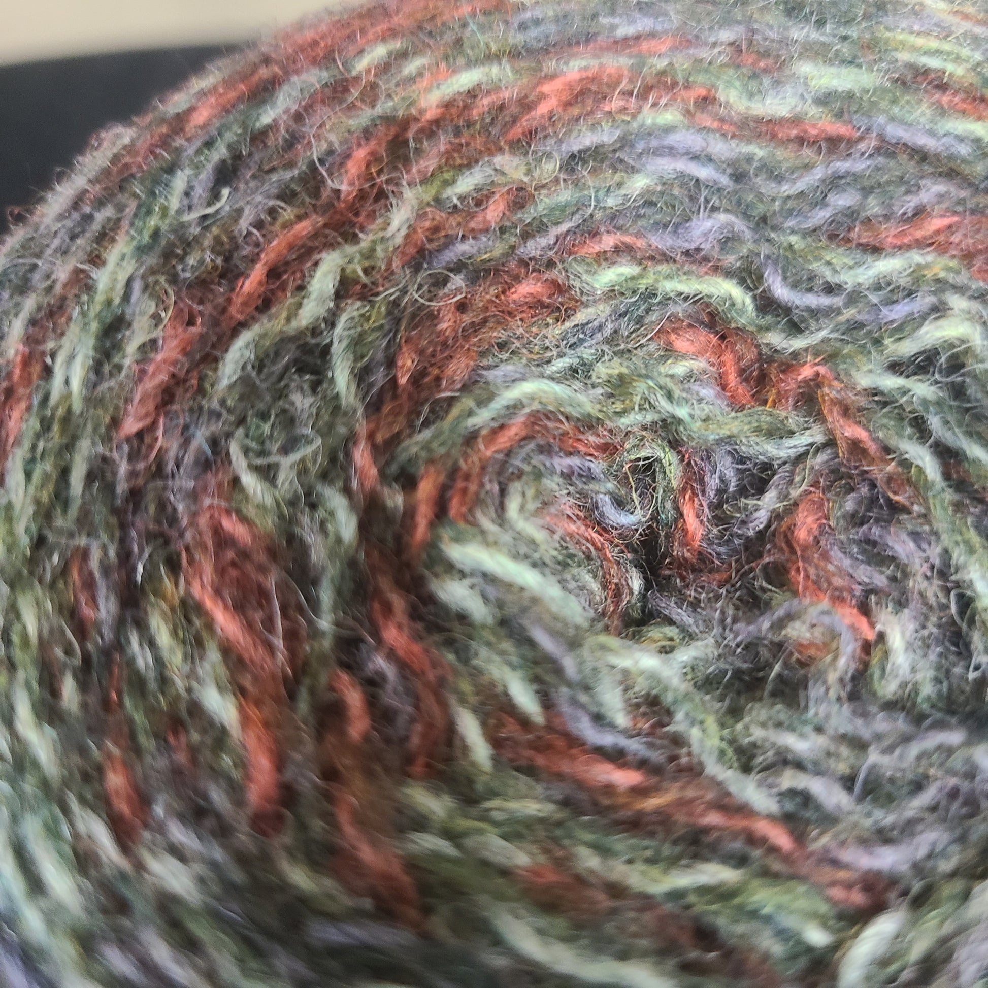 Close-up of a skein of multicolored yarn with green, orange, and gray tones.