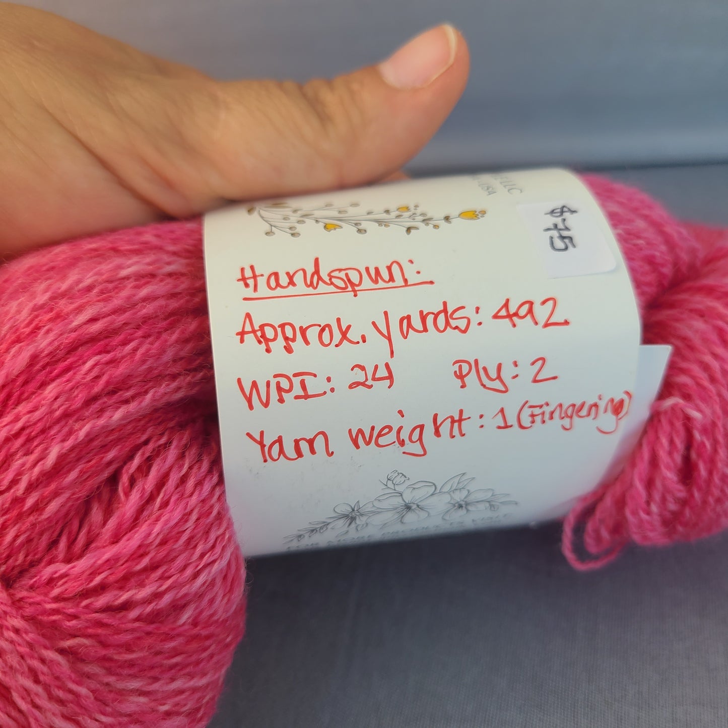 Pink yarn with a label held by a hand against a neutral background