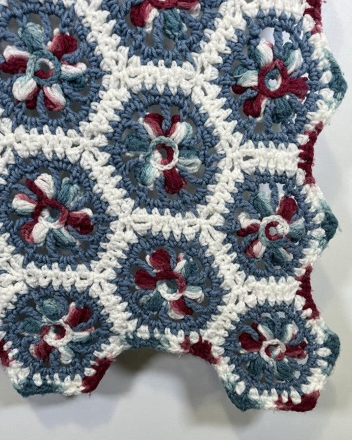 Close-up of a crocheted blanket with blue, white, and red hexagonal patterns.