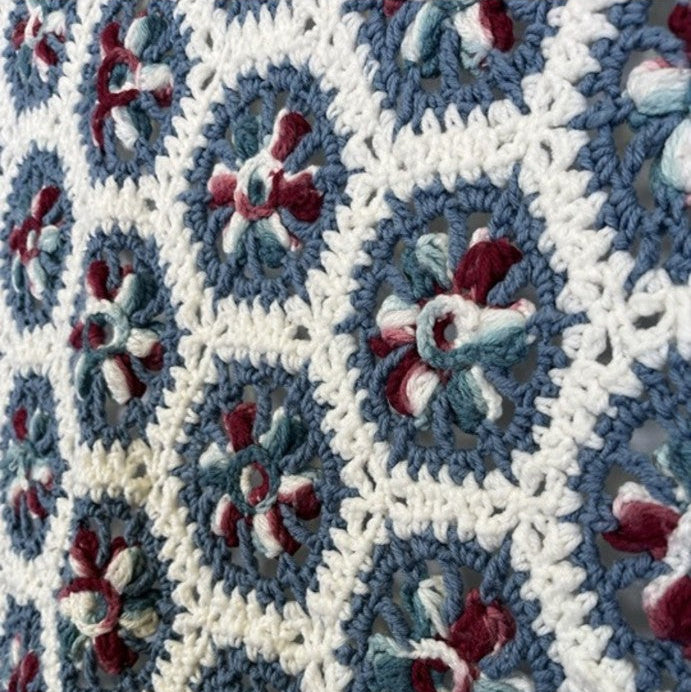Close-up of a crocheted blanket with a geometric pattern featuring blue, white, and red colors.