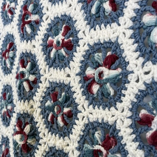 Close-up of a crocheted blanket with a geometric pattern featuring blue, white, and red colors.