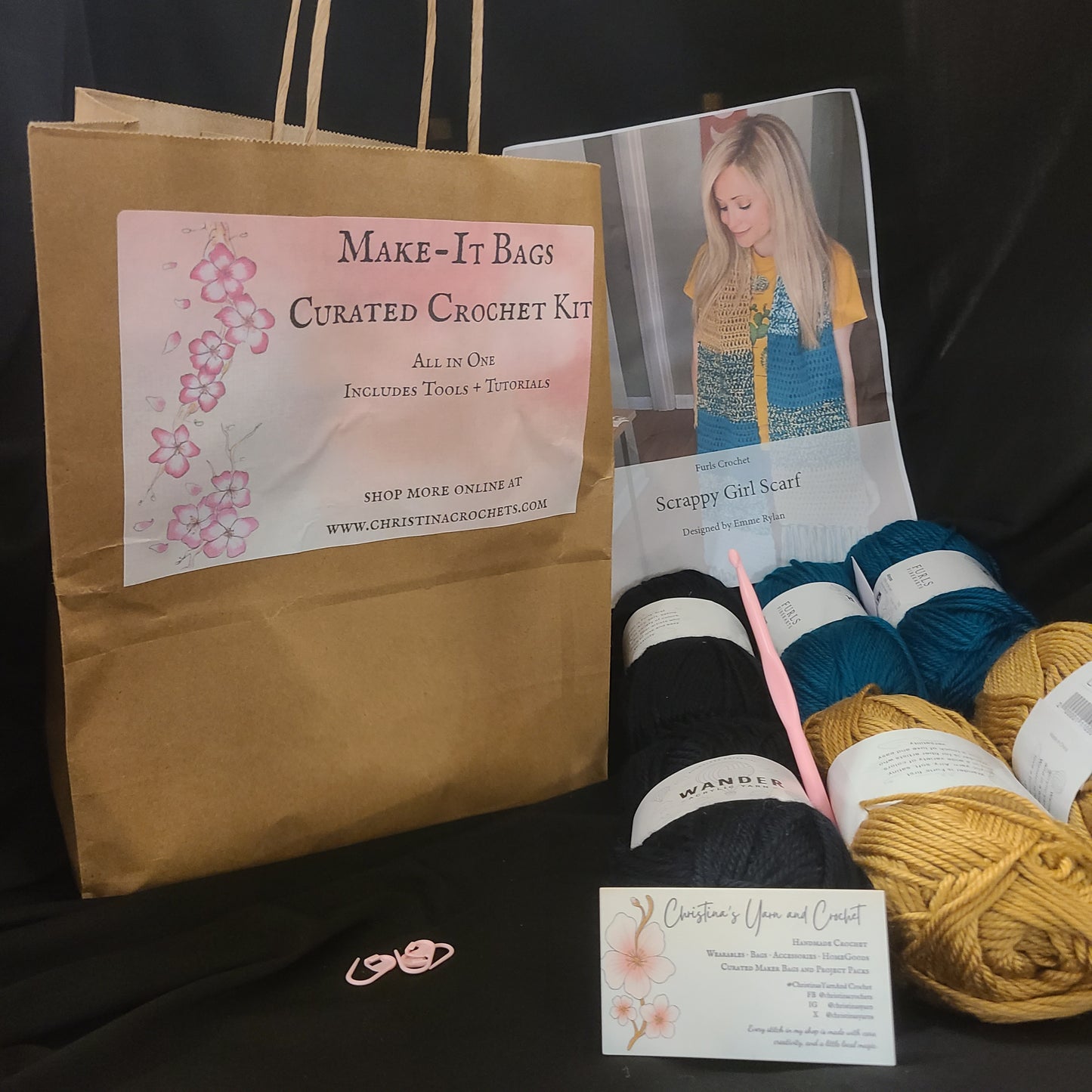 Yarn, knitting needles, and a brown paper bag with promotional material on a black background