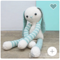 Knitted toy with green hair and blue and white striped outfit on a wooden surface