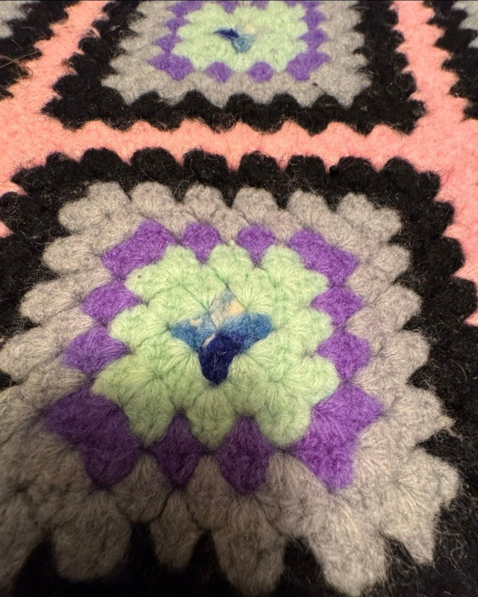 Close-up of a crocheted blanket with a colorful pattern, displayed on a smartphone screen.