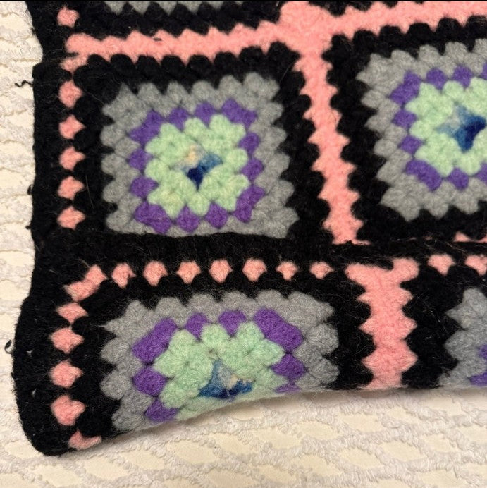 Crocheted blanket with square patterns on a textured surface