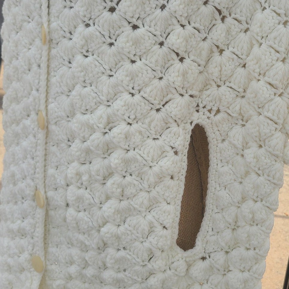 Textured white wall with a small circular opening, outdoor setting with people and chairs.