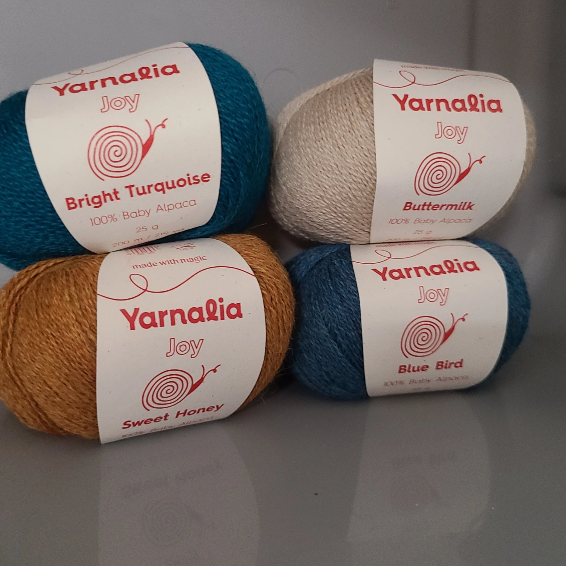 Four balls of yarn with Yarnalia labels Buttermilk, Bright Turquoise, Sweet Honey, Blue Bird