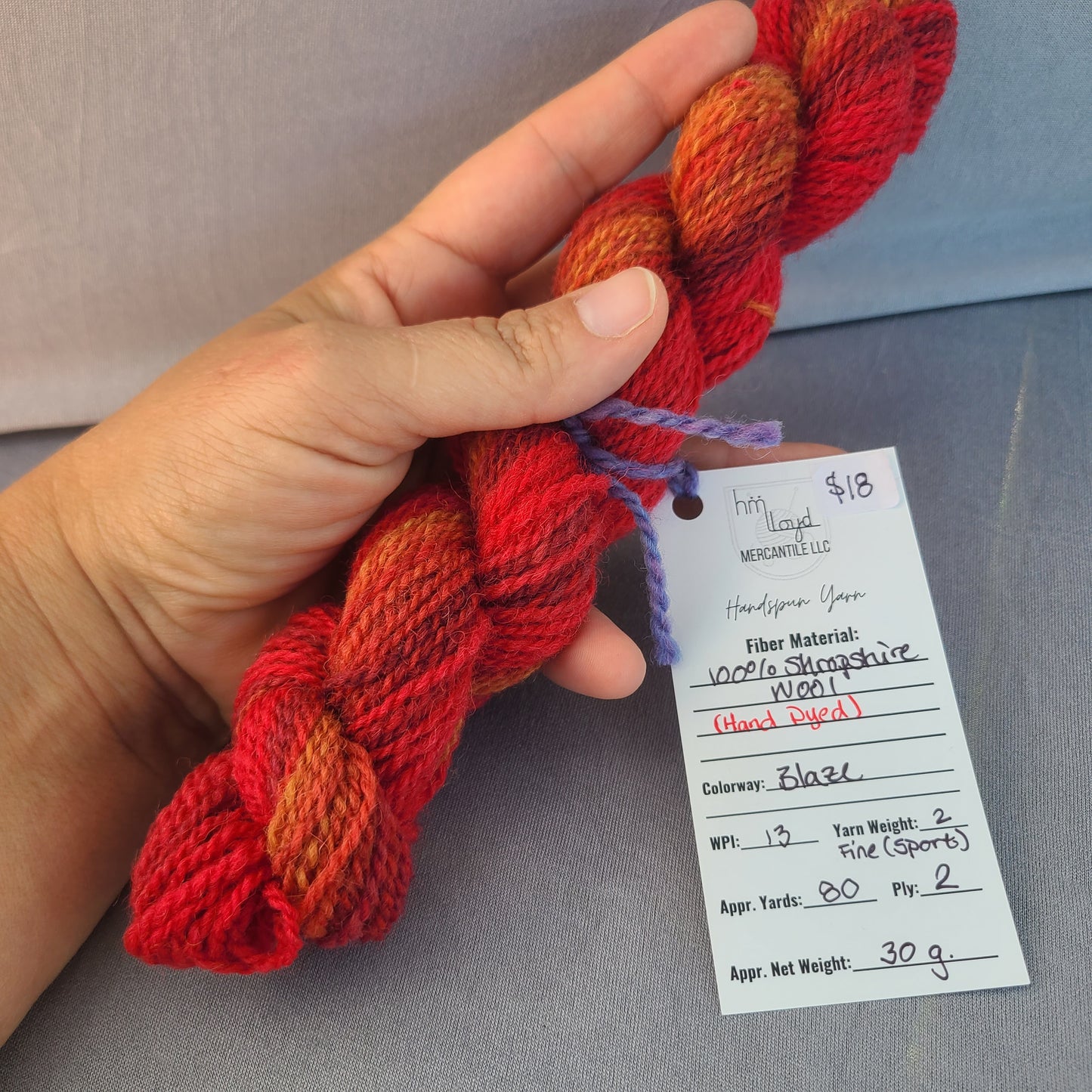 Hand holding red and orange yarn with a label on a gray background
