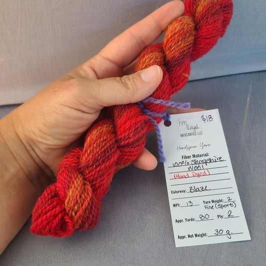 Hand holding red and orange yarn with a label on a gray background