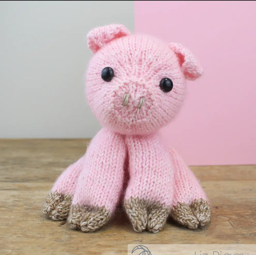 Knitted pink pig toy on a wooden surface with a pink background